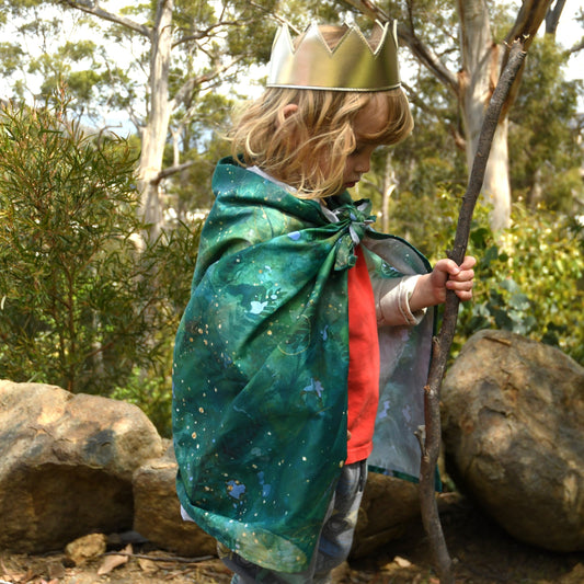 Green forest themed cotton play cloth used as a cape by child during outdoor imaginative play.