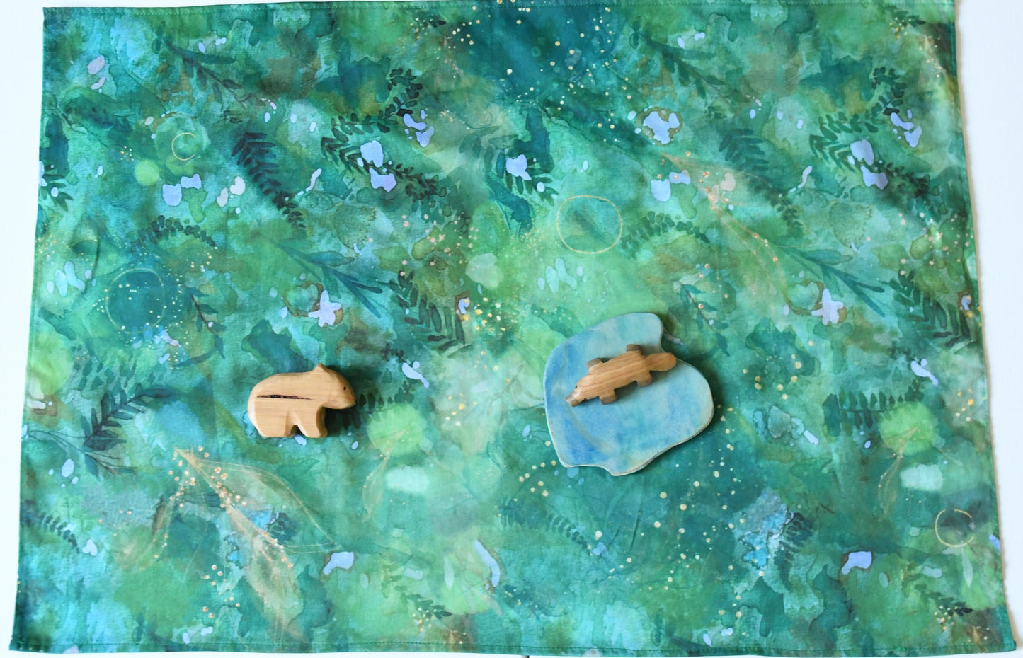 Green forest themed cotton play cloth in open-ended small world play with wooden animal and scenery figurines.