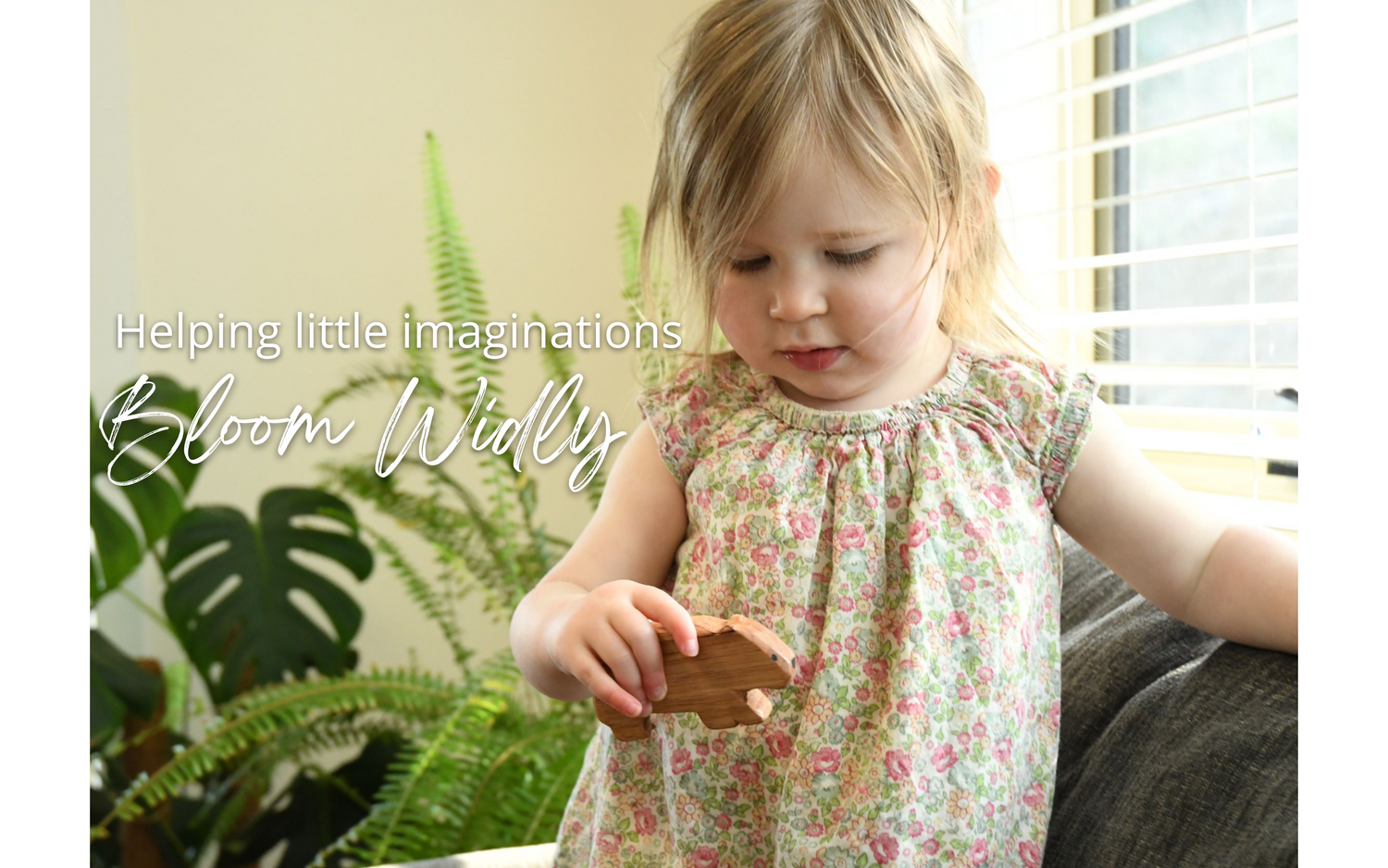 Toddler holding wooden wombat toy handcrafted in Australia from Tasmanian oak with natural oil sealer. The text reads Helping little imaginations bloom wildly.